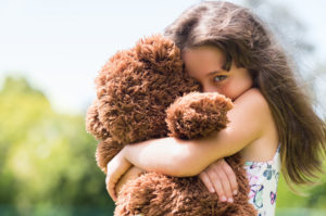 Cute little girl embracing her new teddy bear and looking at camera. Portrait of lovely female child with her peluche outdoor. Little girl playing with her doll.